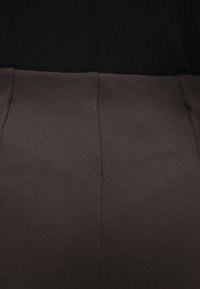 Haut noir à texture lisse, accompagné d'un bas marron en tissu doux. Coutures visibles le long des zones de raccordement.