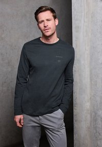 Mörkgrå långärmad skjorta med rund halsringning och en liten textgrafik på bröstet, matchad med ljusgrå byxor. Slät textur.