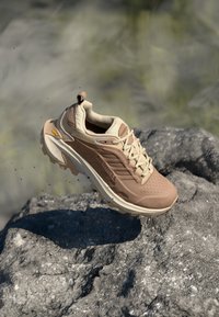 Letvægts brune vandresko med en åndbar mesh-overdel, forstærket tå, gummisål med dybe mønstre og kontrastfarvede beige detaljer.