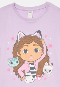 Lilac short-sleeve T-shirt featuring a cartoon character with curly hair in a pink hoodie, surrounded by three cartoon cats and pink stars.