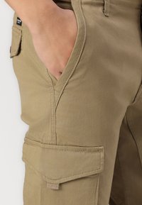 Khaki cargobroeken hebben meerdere zakken en zijn gemaakt van een zacht, duurzaam stof. Het ontwerp bevat gestikte naden en een lichte glans.