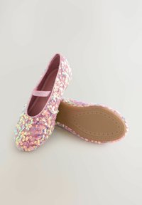 Scarpine per bambini rosa decorate con paillettes luccicanti; una scarpa mostra la parte superiore glitterata, mentre l'altra mostra la suola in gomma con motivi a stella.