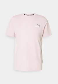Camiseta de algodón rosa con mangas cortas, cuello redondo y un logo negro de Puma en el lado izquierdo del pecho. Presenta un dobladillo recto y una abertura lateral.