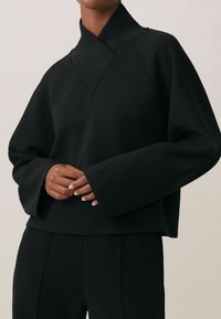 Czarny, oversize sweatshirt z wysokim kołnierzem, szerokimi rękawami i skróconym krojem. Gładka tekstura i minimalne detale szwy widoczne.