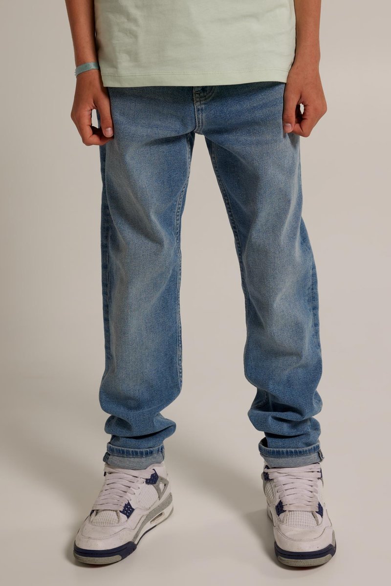 Jeans azzurro chiaro, modello relaxed-fit con una texture sbiadita, abbinati a sneakers bianche con accenti navy e dettagli in rete.