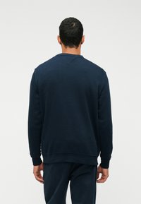 Sweatshirt azul-marinho com gola redonda, mangas longas e punhos canelados. Apresenta uma costura em V nas costas. Tecido macio e texturizado.