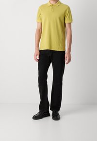 Polo jaune avec col et trois boutons, associé à un jean en denim noir et des chaussures noires. Texture lisse, coupe ajustée.