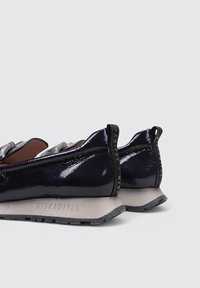 Zapatos de charol azul marino con un diseño elegante, suela de goma gris en contraste y detalle del logo visible en el talón trasero.