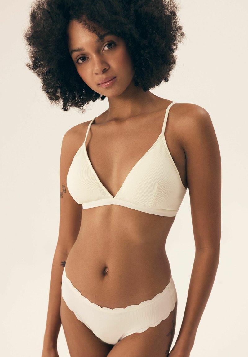 Light beige ribbed triangle bralette with adjustable straps, paired with matching scalloped-edge bikini bottoms. Soft texture, simple design.