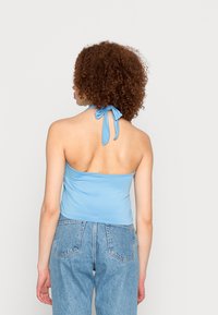 Top halter azul claro com um fecho em nó nas costas, feito de um tecido suave. Combinado com jeans de cintura alta.
