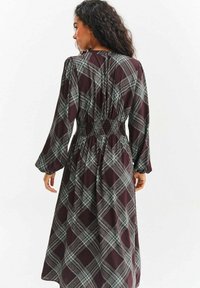 Bordowa sukienka z długim rękawem w zielono-białą kratkę. Posiada marszczoną talię i luźny krój. Miękki materiał z lekkim połyskiem.