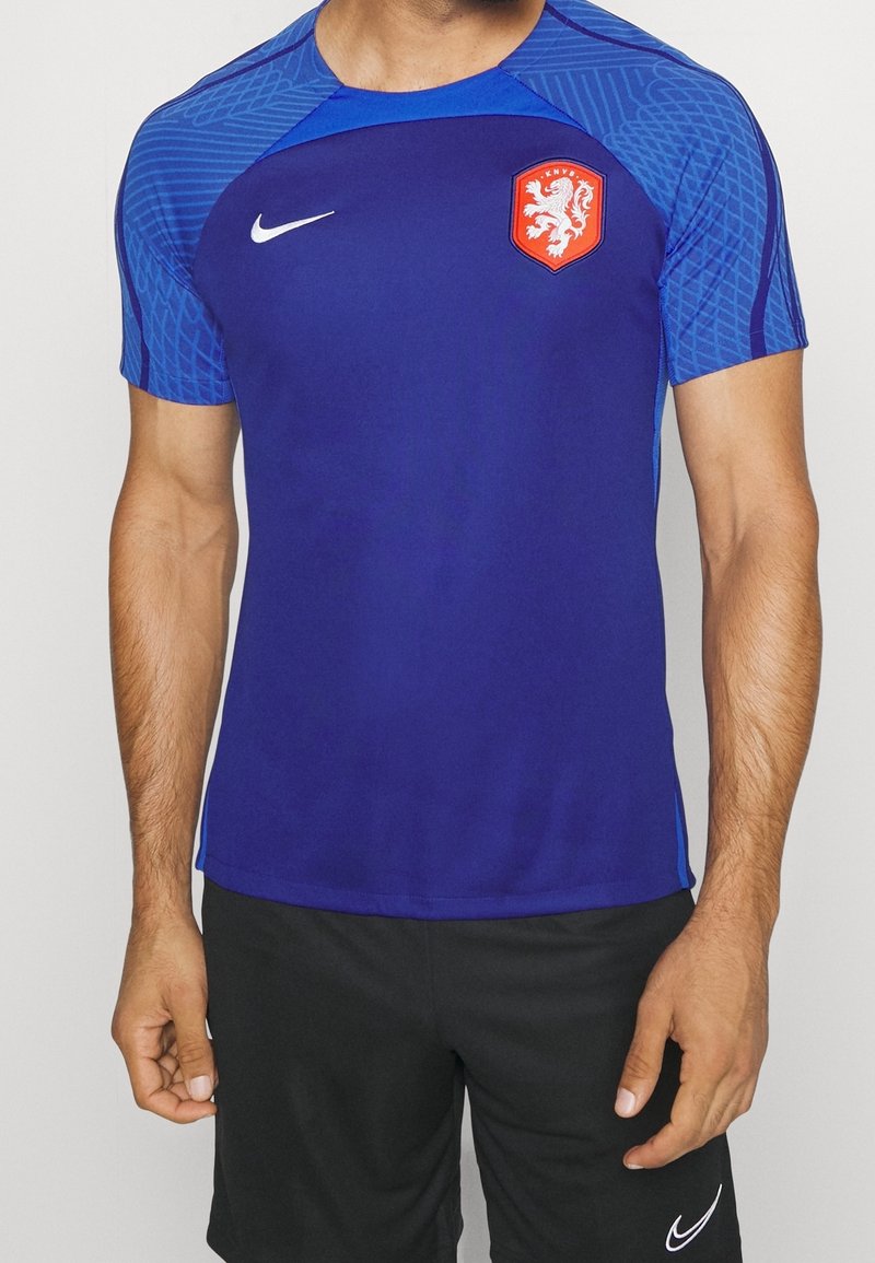 Camisa atlética de color azul royal con mangas cortas, que presenta un diseño texturizado en el hombro azul y un logo de cresta roja. Logo de Nike en blanco en el pecho.