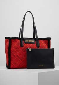Röd toteväska med svart fluffig kant, prydd med texten "LOVE MOSCHINO". Inkluderar en avtagbar svart ficka med guld dragkedja och logotyp.