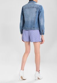 Jeansjacka i ljusblå färg med klassisk skärning, framfickor och knappstängning, kombinerad med randiga shorts och vita ankelstövlar.