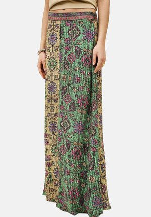 Jupe longue avec un patchwork vertical de motifs floraux verts et beiges, portée avec un top court beige, montrant les mains et le ventre.