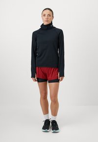 Langærmet, marineblå atletisk top med høj krave, parret med røde shorts med sort talje. Sorte træningssko og hvide sokker.