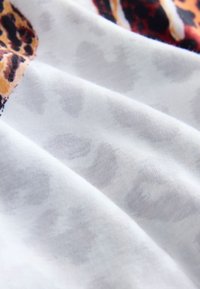 Lichtgewicht stof met een witte basis en een subtiele dierenprint in beige en bruine tinten, wat zorgt voor een dynamische textuur en patroon.