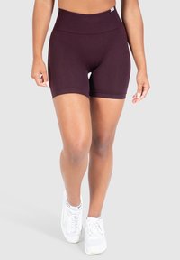 Pantalones cortos deportivos burdeos con una cintura alta. Hechos de tela elástica, con una textura suave y dobladillos acampanados. Se llevan con zapatillas blancas.