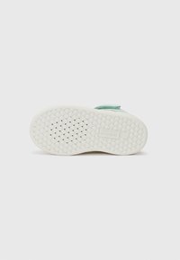 Light green shoe sole with a textured rubber surface, featuring a diamond pattern and a prominent logo on the heel.
