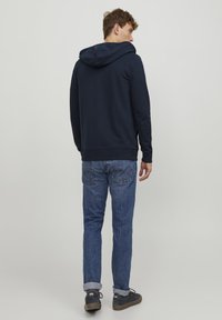 Marineblå pullover hoodie med snoretræk i hætten, parret med lyseblå denim jeans. Sættet har et afslappet design og en tætsiddende silhuet.