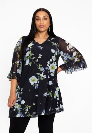 Tunique noire à motifs floraux avec des fleurs bleues et vertes, décolleté en V et manches en organza à volants, assortie à des leggings noirs.