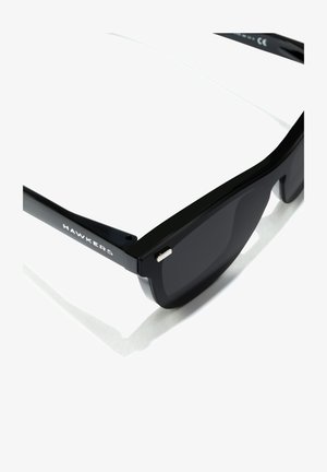 Black sunglasses featuring a sleek plastic frame and dark lenses, with "HAWKERS" printed on the arm and a silver accent on the hinge.