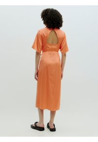 Lange, rugloze oranje satijnen jurk met korte mouwen en een getailleerde taille, gecombineerd met zwarte platte sandalen. Gladde textuur en vloeiende stijl.