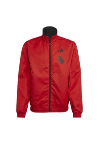 Veste zippée rouge avec une texture unie, accents de logo noirs, col montant et poignets élastiques. Fabriquée en matériau léger et brillant.