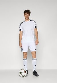 Hvid Adidas fodboldoutfit med en kortærmet trøje med sorte accenter, matchende shorts og knælange strømper; sorte fodboldstøvler og en fodbold.