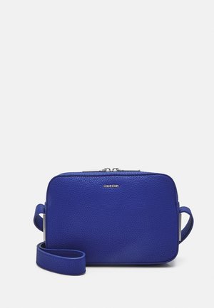 Mała prostokątna niebieska skórzana torebka na ramię z ziarnistą fakturą, srebrnym zamkiem błyskawicznym i logo Calvin Klein z przodu.