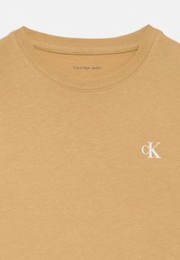 Kamelfarget Calvin Klein Jeans T-skjorte med rund hals og liten hvit "cK" logo på brystet.