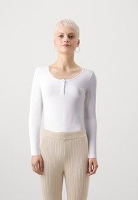 Hvit langermet bodysuit med scoop hals og knappestenging foran, kombinert med beige ribbestrikkede bukser med høy midje.
