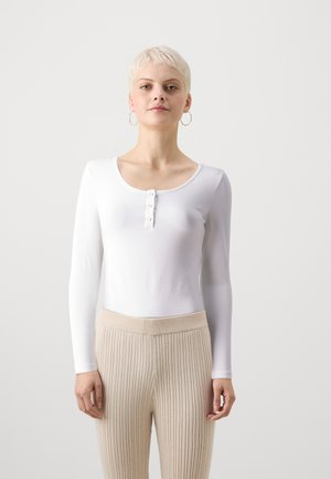 Body blanco de manga larga con escote redondeado y cierre de botones en la parte delantera, combinado con pantalones de tiro alto de canalé beige.