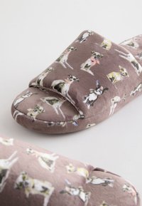 Pruunid sametised sussid väikeste joonistatud prillidega ja salli kandevate koerte mustriga heledal taustal.