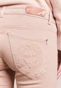 Světle růžové džíny z denimu s přišitými zadními kapsami se znakem "PATRIZIA PEPE" a detailním vyšíváním. Součástí je kožená štítek na pase.
