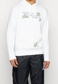 Vit hoodie med gröna löv och tecknad karaktärsgrafik, framficka med känguru-design och justerbar dragsko i huvan. Mjuk bomullsmaterial.