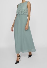 Une robe sans manches, longue jusqu'aux chevilles, de couleur vert menthe avec un corsage en dentelle et une jupe en mousseline fluide. Elle présente un col rond et une texture subtile.
