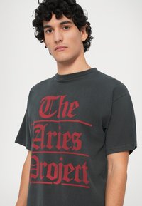 Grafička crna majica kratkih rukava s odvažnim crvenim natpisom "The Aries Project". Ima okrugli izrez i izrađena je od pamuka.