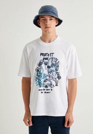 Hvid bomulds T-shirt med en blå og sort maritimt grafisk design med tekst. Korte ærmer og rund hals.