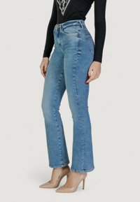 Jeans in denim leggeri a vita alta, di colore azzurro, con gamba a sbuffo, caratterizzati da una chiusura frontale con bottone e due tasche posteriori, abbinati a tacchi alti beige.