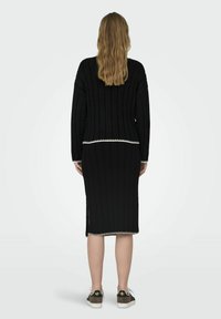 Robe noire en maille côtelée avec des manches longues, fentes sur les côtés et bordure blanche à la taille. Associée à des baskets noir et blanc.