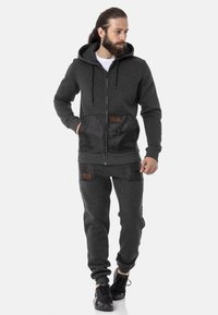 Gray hoodie with a zipper and hood, featuring black satin panels and pockets. Paired with matching gray joggers, both in a soft fabric.