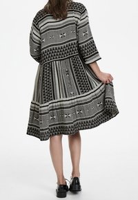 Schwarz- und grau gemustertes Kleid mit gestuften Design, 3/4-Ärmeln und geometrischen Motiven. Fließender Stoff mit knielangem Saum.