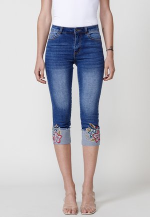Blue denim capri jeans featuring floral embroidery on the cuffs, with a mid-rise waist and a slim fit design.