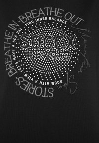 Camiseta negra con texto de purpurina plateada en un diseño circular. Incluye frases como "INSPIRA" y "SOCXX," con acentos punteados.