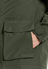 Olivgrön Didriksons-jacka med texturerad yta, som har en stor fickklaff, justerbara ärmar och en diskret logotyp på bröstet.