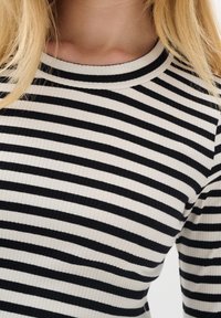 Mustat ja valkoiset raidalliset ribbikudotut neuleet, joissa on pyöreä pääntie. Kangas on tekstuuriltaan tasaisesti vaakasuorilla raidoilla, mikä antaa tiukan istuvuuden.