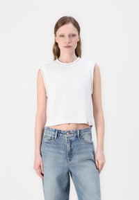 Hvit utenermet strikket crop topp med rund halsutskjæring, stylet med lyseblå høyhøydde jeans med avslappet passform og falmet tekstur.