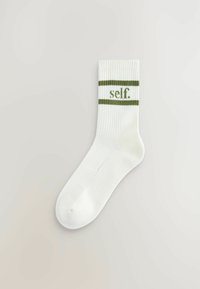 Bílá bavlněná ponožka se zelenými vodorovnými pruhy a slovem "self." uprostřed. Hladký vzor v horní části pro lepší uchopení.