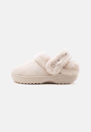 Chaussure beige à enfiler avec semelle épaisse et bride douce réglable autour du talon, dotée d'une doublure douce et moelleuse pour le confort.